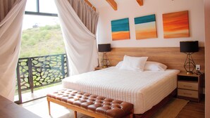 Une chambre avec un grand lit, un banc, un balcon avec vue et des œuvres d’art accrochées au mur.