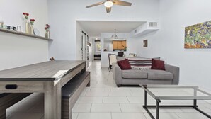 A modern living room with a grey sofa, a glass coffee table, and a wooden dining table.