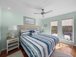 Un dormitorio con cama, mesitas de noche, ventilador de techo y vistas al exterior.