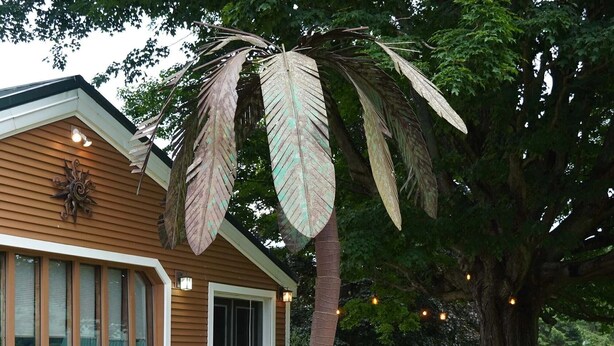 A house with a patio area featuring wicker furniture, a stone wall, and a palm tree.