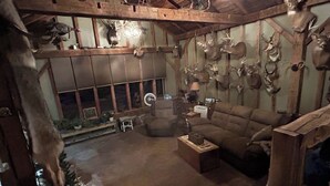 A rustic room with a wooden ceiling, a brown sofa, a small table, and various animal heads mounted on the walls.