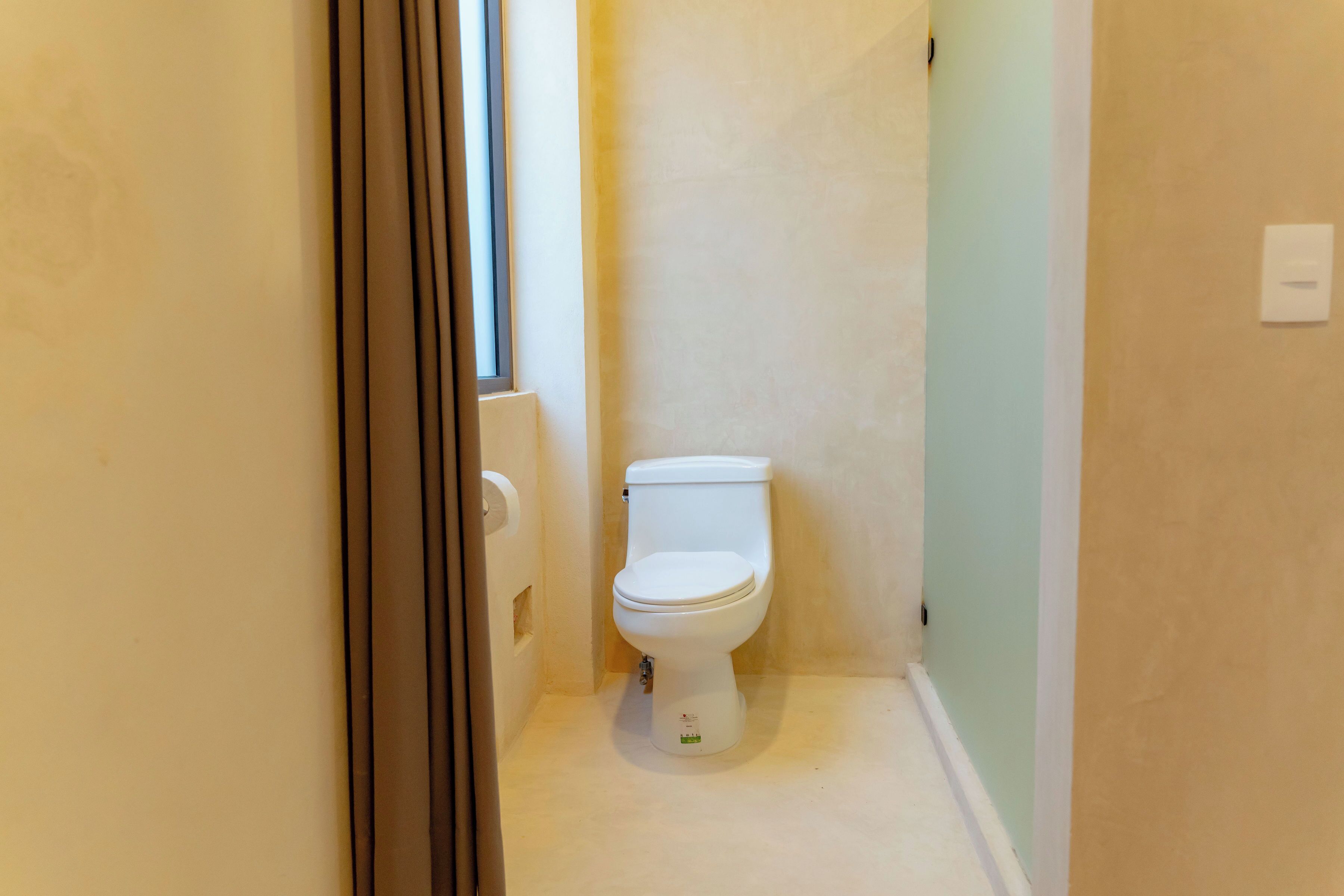 Un baño pequeño y estrecho con un inodoro, un rollo de papel higiénico y una ventana.