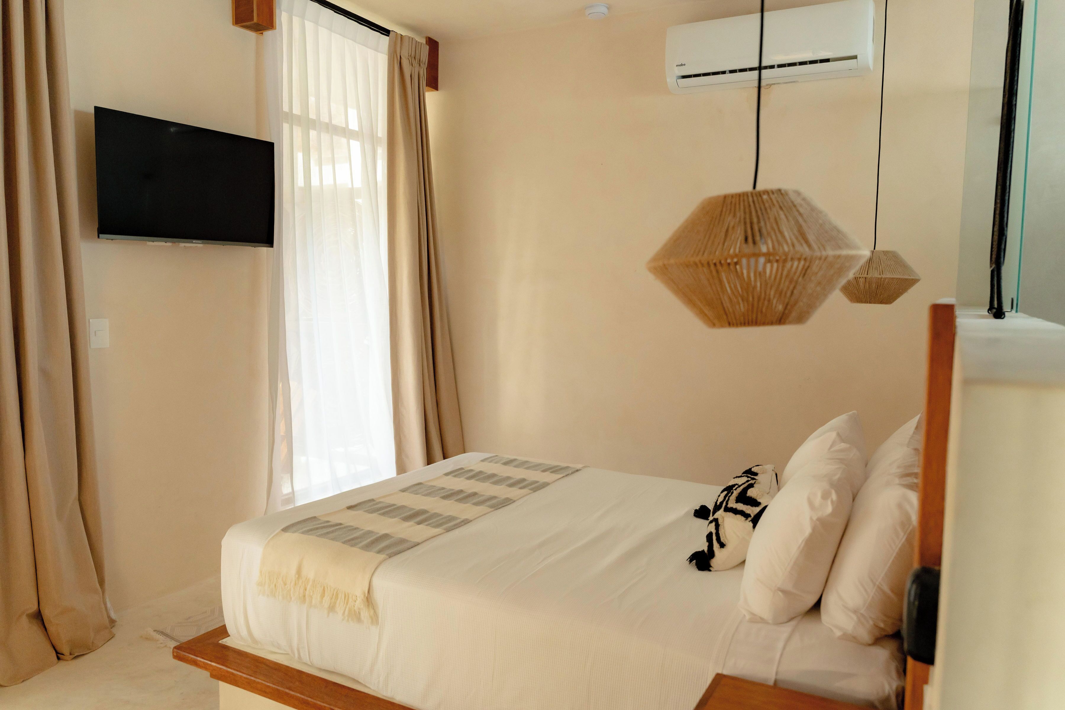A bedroom with a bed, a mounted TV, an air conditioning unit, and a window with curtains.