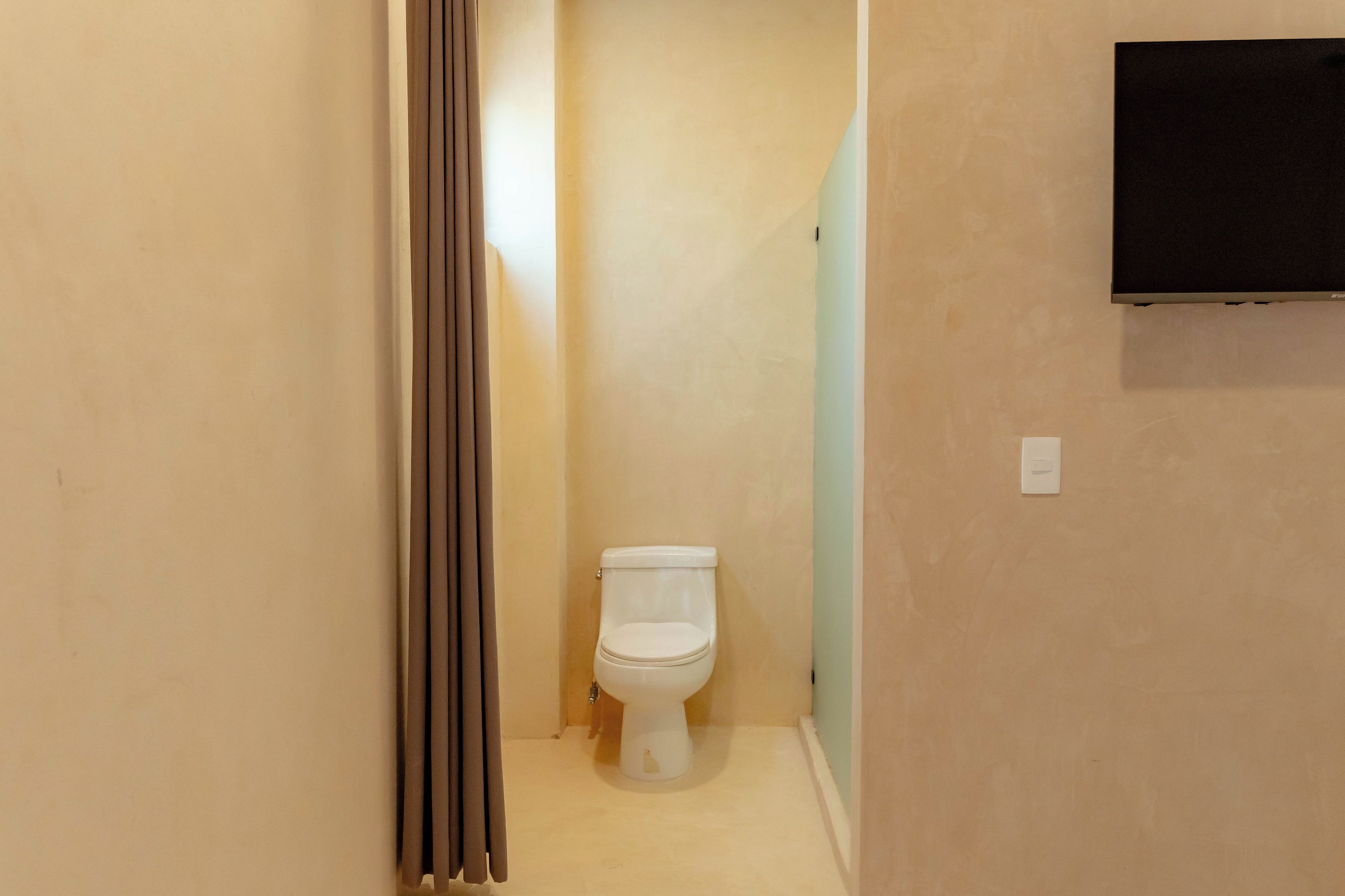 Une petite salle de bain comprenant des toilettes, un rideau de douche et un téléviseur fixé au mur.