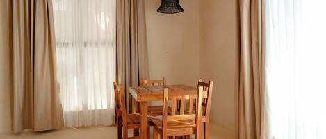 A dining area with a wooden table and chairs, beige curtains, and a hanging light fixture.