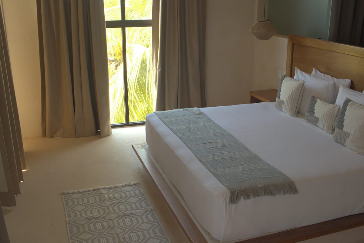 Un dormitorio con una cama grande, una mesita de noche, una alfombra estampada y vistas a palmeras a través de la ventana.