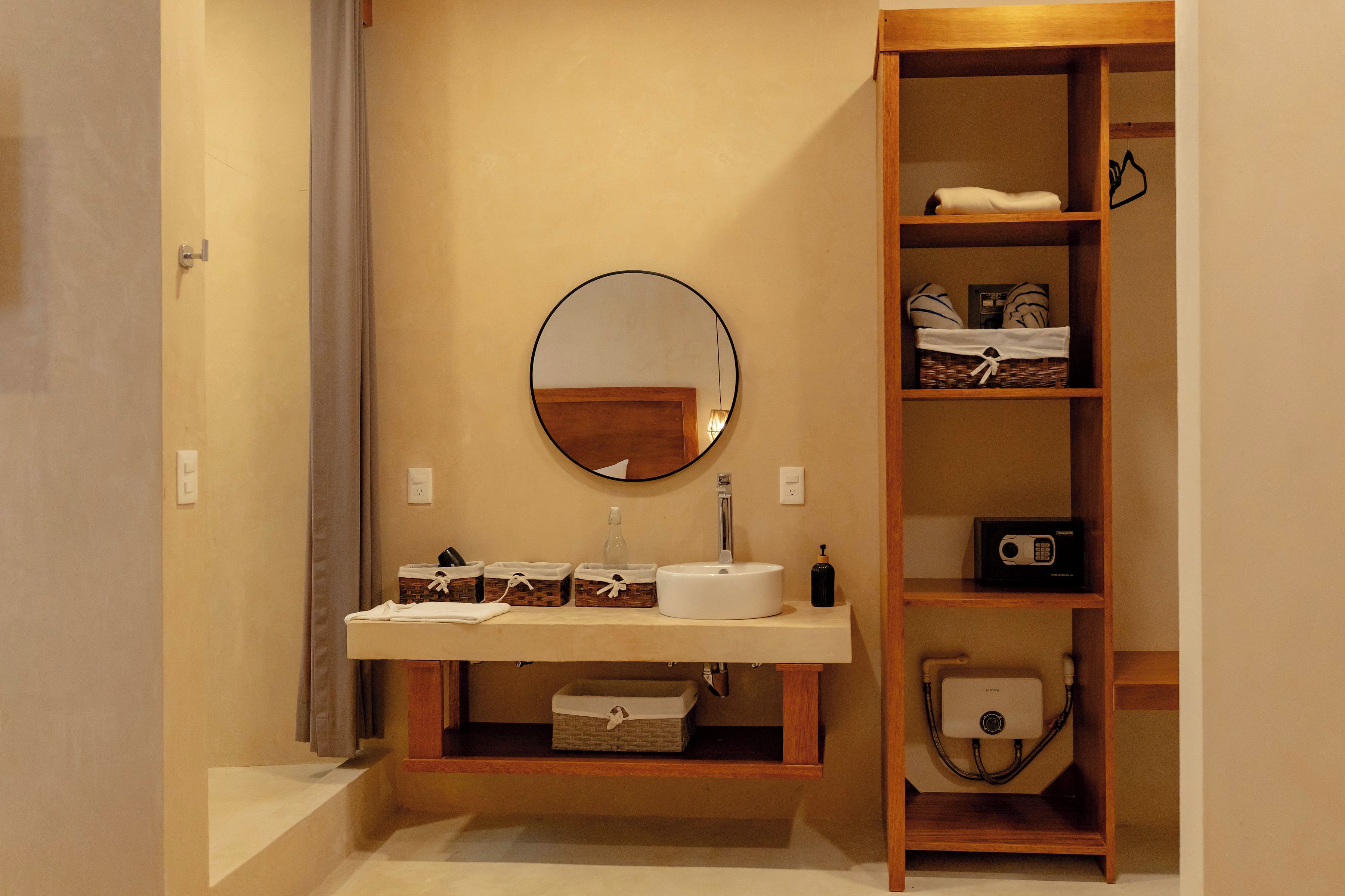 Un baño con un espejo redondo, un lavamanos y un estante de madera con diversos objetos.