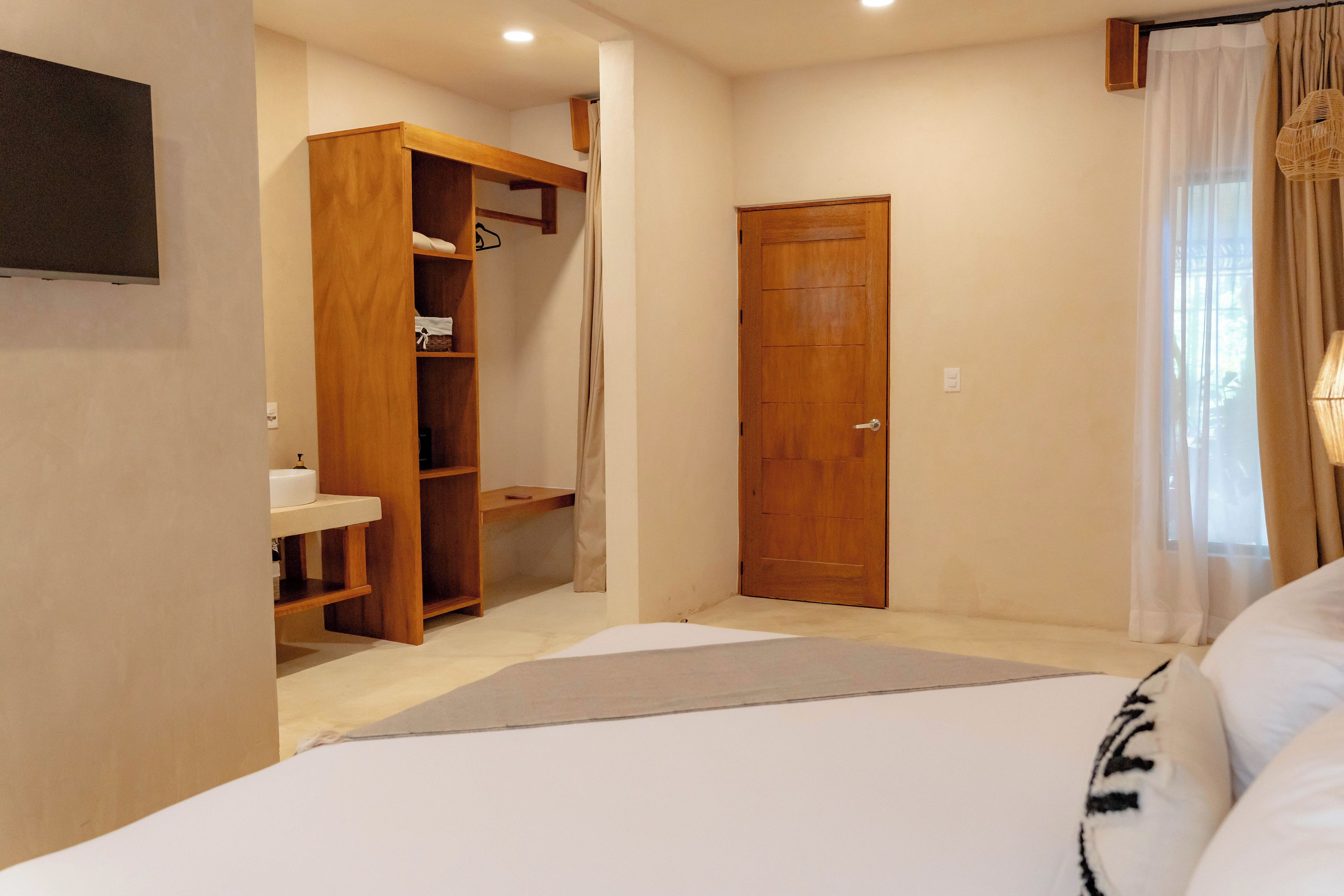 Un dormitorio con cama, armario de madera, puerta y ventana con cortinas.