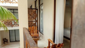 Un balcón con una silla de madera, una mesita y una silla de mimbre.