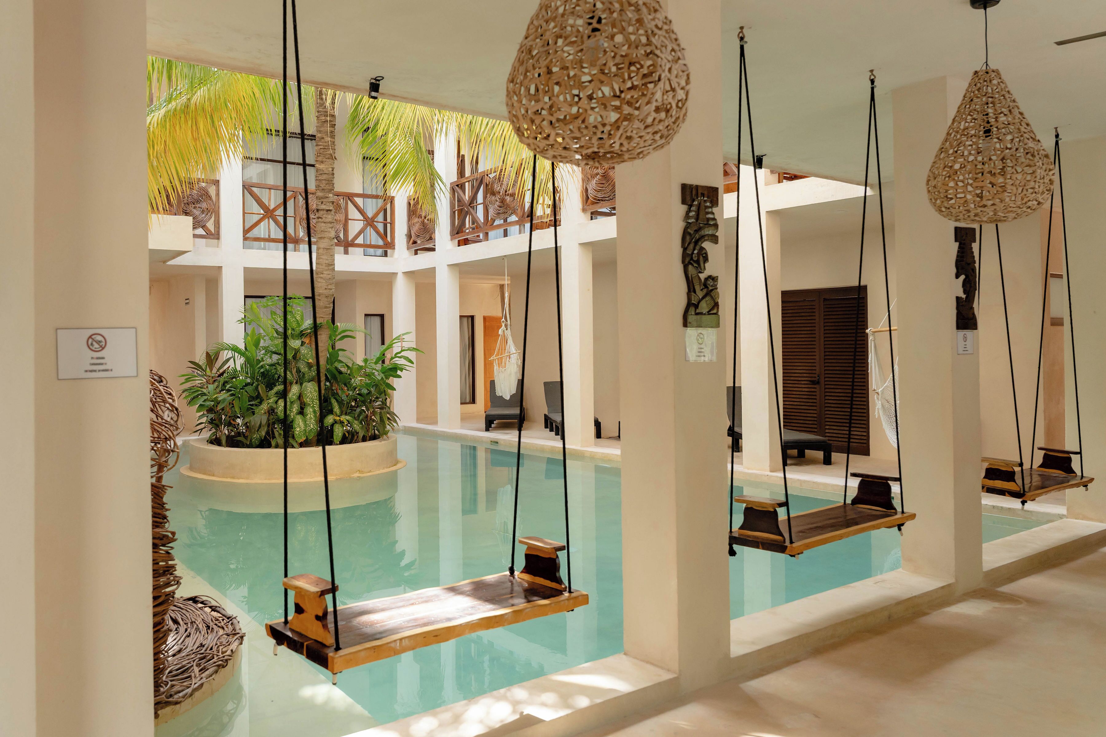 Uma área de piscina com cadeira de balanço, luminárias de rattan suspensas e uma planta no centro.