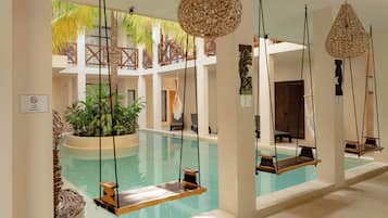 Uma área de piscina com cadeira de balanço, luminárias de rattan suspensas e uma planta no centro.