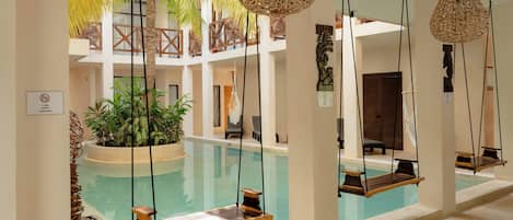 A pool area with a swing chair, hanging rattan lamps, and a plant in the center.