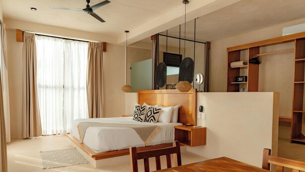 Una habitación de hotel con cama, mesita de noche, espejo, armario y una mesa de comedor.