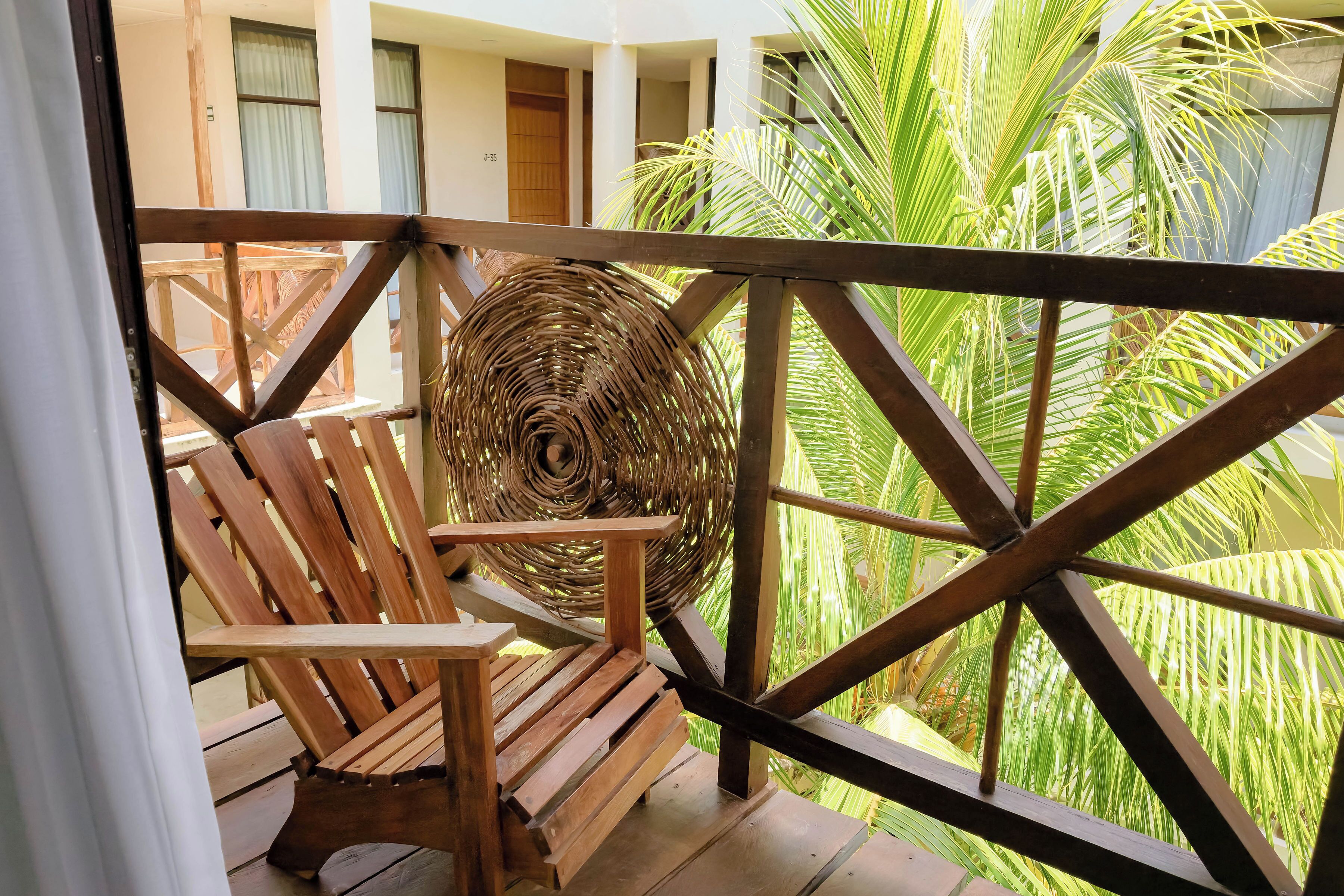 Una silla de madera y una cesta tejida en un balcón con vista a follaje verde.