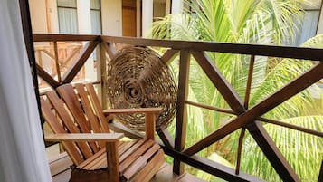 Una silla de madera y una cesta tejida en un balcón con vista a follaje verde.