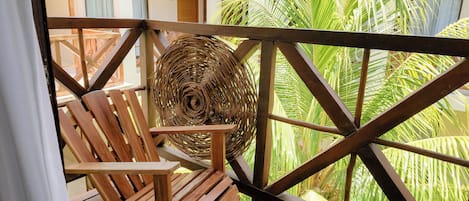 A wooden chair and a woven basket on a balcony with a view of green foliage.
