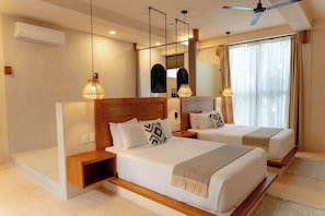Habitación de hotel con dos camas, ventilador de techo, aire acondicionado y un gran ventanal con cortinas.
