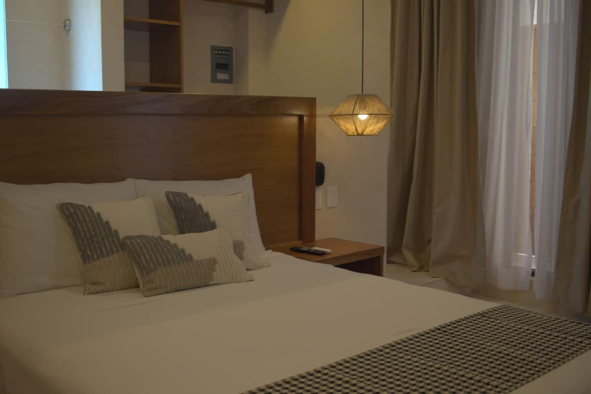 Una habitación de hotel con una cama grande, cabecera de madera y una mesita de noche con lámpara.