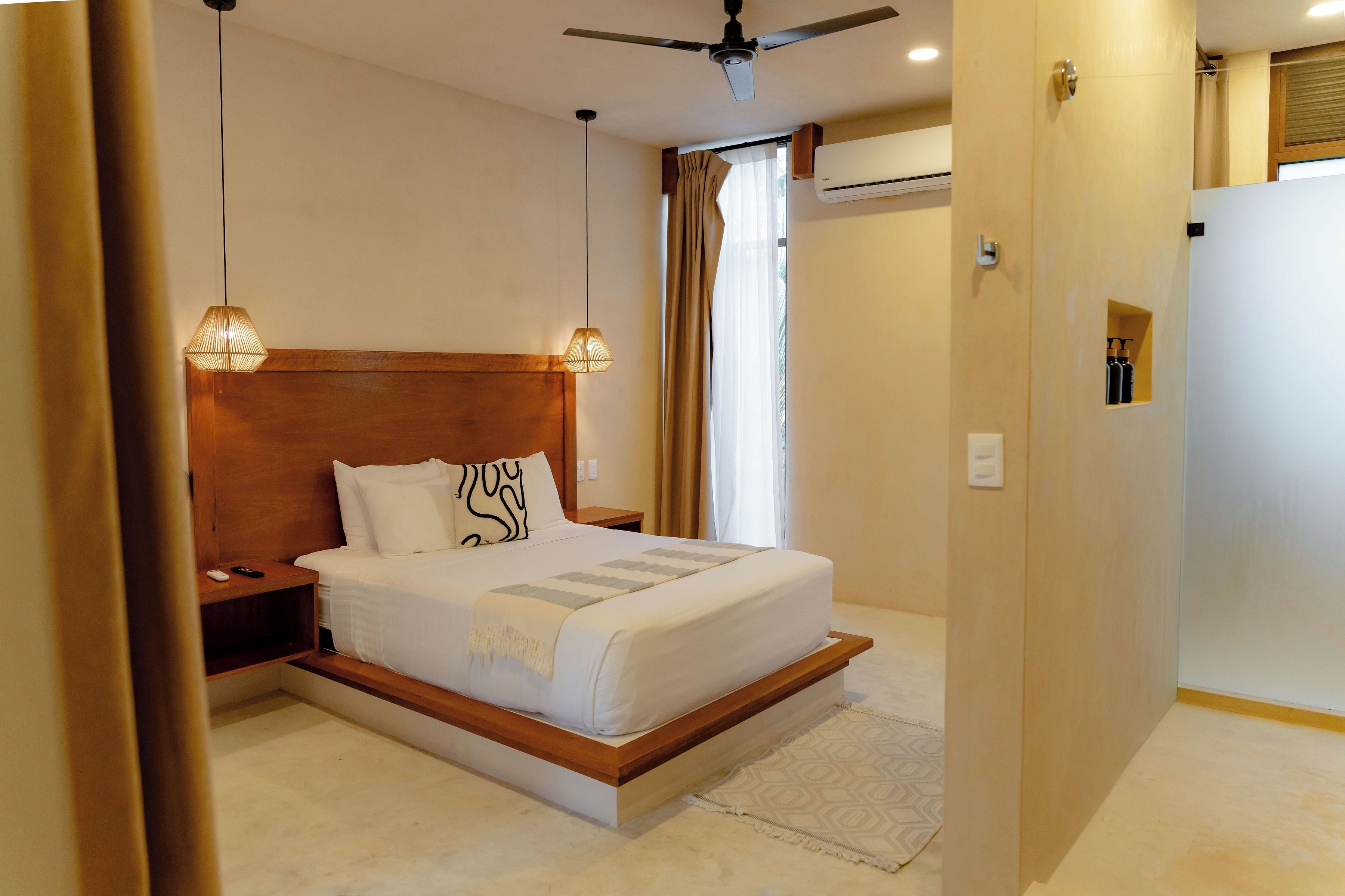 Ein Hotelzimmer mit einem großen Bett, einem Holzkopfstück, einem Nachttisch und einem Deckenventilator sowie einer Klimaanlage.