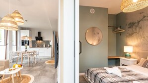 A modern hotel room with a bed, bedside table, and a view of the kitchen and dining area.