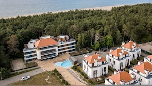 A multi-story hotel with a swimming pool, located near a beach and surrounded by trees.