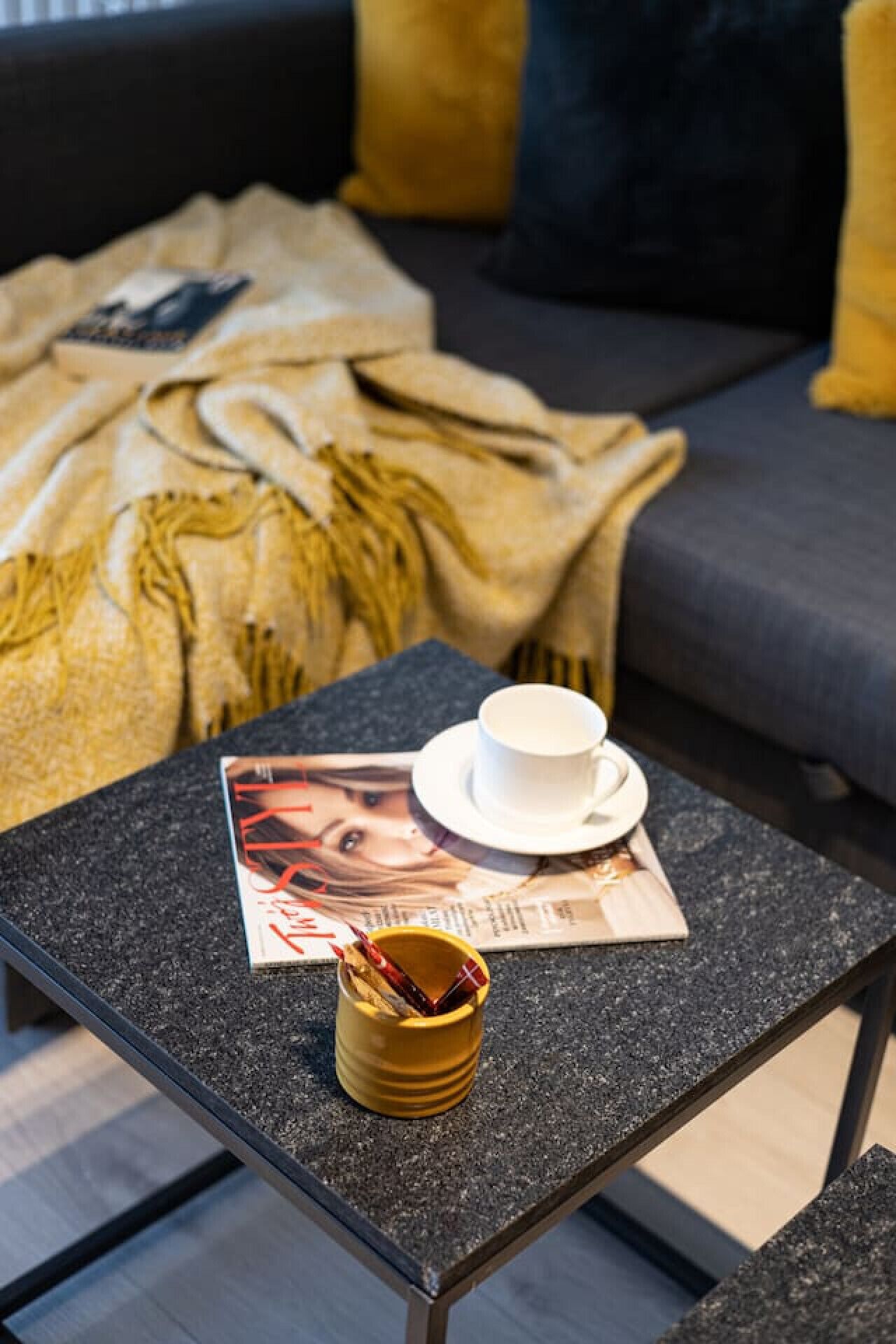 Une petite table avec une tasse et une soucoupe, un magazine et une tasse jaune.