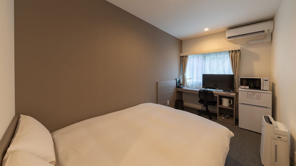 A hotel room with a large bed, a desk with a computer, a television, and a refrigerator.