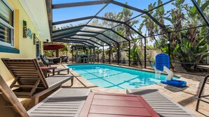 A covered outdoor swimming pool with lounge chairs and a shaded area.