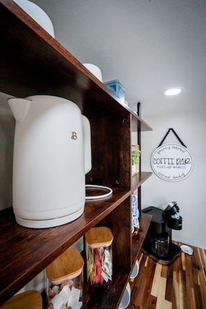 A kitchen area with a coffee machine, a kettle, and a coffee bar sign on the wall.