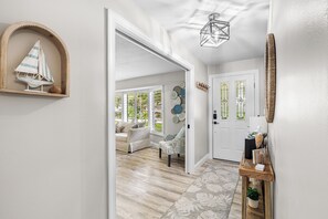 A hallway with a wooden floor, a white door, and a small table with a plant. - Twin Oaks Luxury Heated Pool and Caribbean Tiki Bar Near Indian Rocks Beach (Largo)