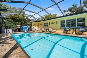 A swimming pool with a glass enclosure, sun loungers, and a covered patio area.