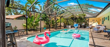 Una piscina al aire libre con zona techada, sillas de descanso y un flotador con forma de flamenco.
