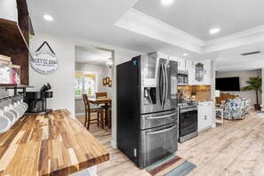 A modern kitchen with a stainless steel refrigerator, a coffee station, and a dining area with a wooden table and chairs.