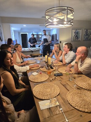 A group of people seated around a wooden table with woven placemats, a candle, and a bottle of wine.