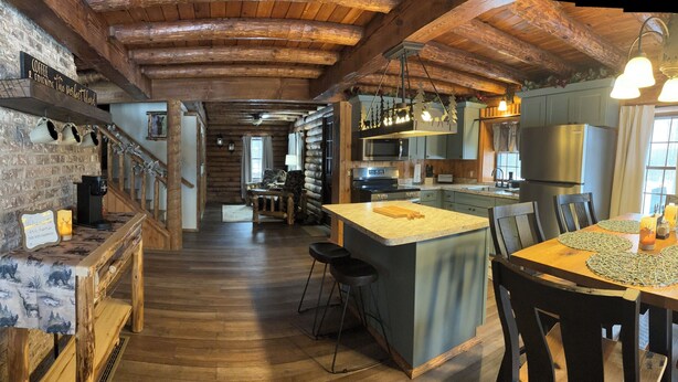 Cocina rústica con vigas de madera, una isla central, taburetes de bar y una mesa de comedor con posavasos.