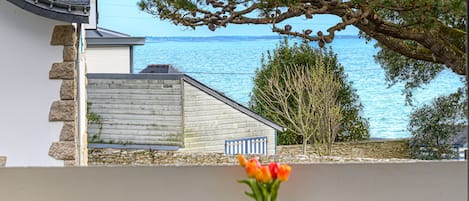 A seaside view with a wooden building, a stone wall, and a table with a vase of flowers.