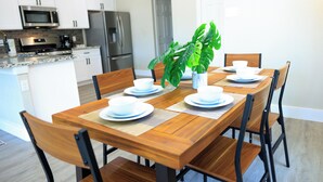 Une cuisine moderne avec des meubles blancs, des appareils en acier inoxydable et une table à manger en bois pour quatre personnes.