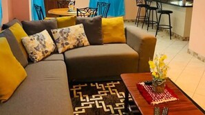 Ein Wohnzimmer mit einer Couch, einem Couchtisch und einem gemusterten Teppich. Es gibt einen Essbereich mit Stühlen und einem Tisch.