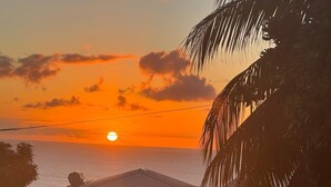 Ein Sonnenuntergang über dem Meer mit einem Haus und einer Palme im Vordergrund.