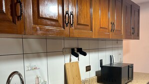 A kitchen with wooden cabinets, a stainless steel sink, a microwave, and a cutting board.