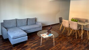 A modern living room with a grey sofa, a glass coffee table, and a dining area with a glass table and chairs.
