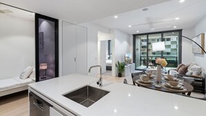 Une cuisine moderne dotée d’un îlot central, d’un coin repas avec une table pour quatre personnes et d’une vue sur un balcon aménagé avec du mobilier d’extérieur.