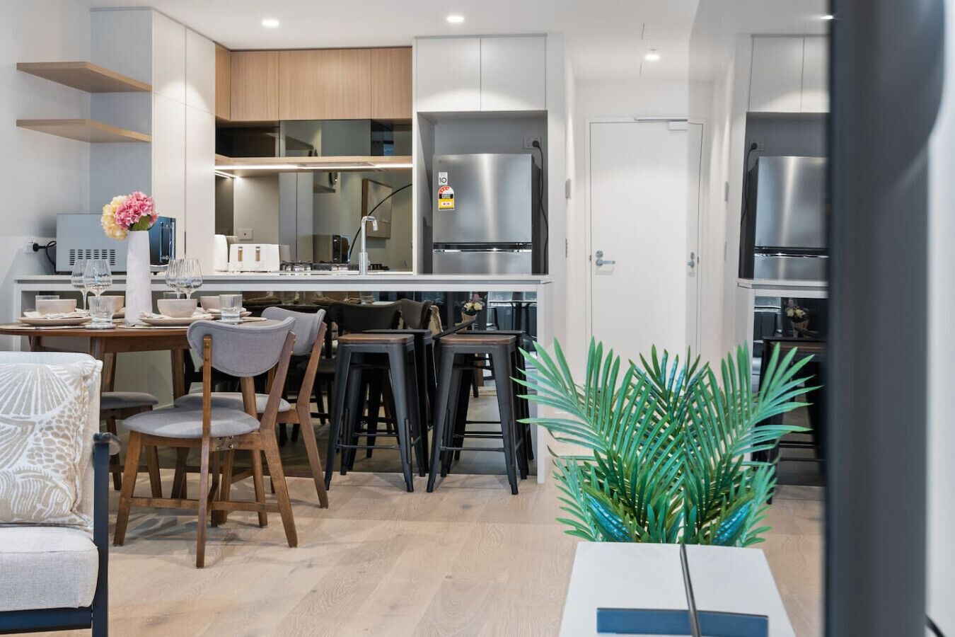 A modern kitchen with white cabinets, stainless steel appliances, and a dining area with wooden chairs and a table.