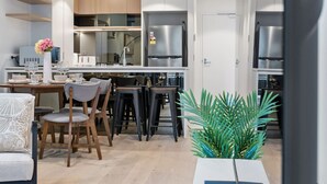 Une cuisine moderne avec des meubles blancs, des appareils en acier inoxydable et un coin repas comprenant des chaises et une table en bois.