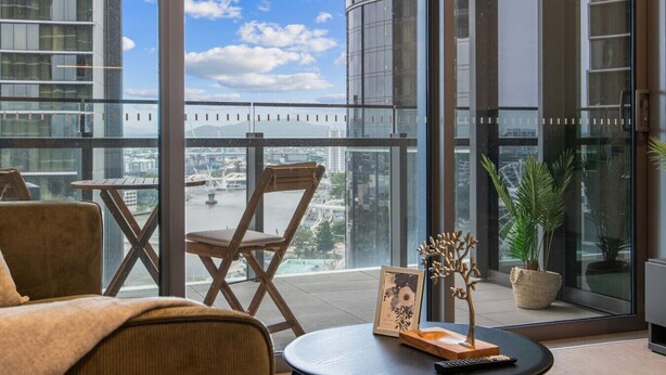 Una habitación moderna con un ventanal amplio, una silla de madera, una mesita pequeña y una planta decorativa.