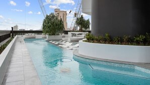 Una piscina en la azotea con vistas despejadas al horizonte de la ciudad, rodeada de arquitectura moderna y vegetación.
