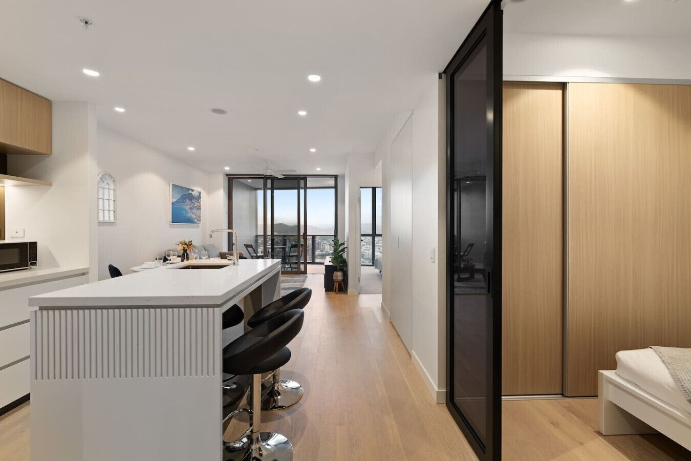 A modern kitchen with a central island, bar stools, and a view to a balcony.