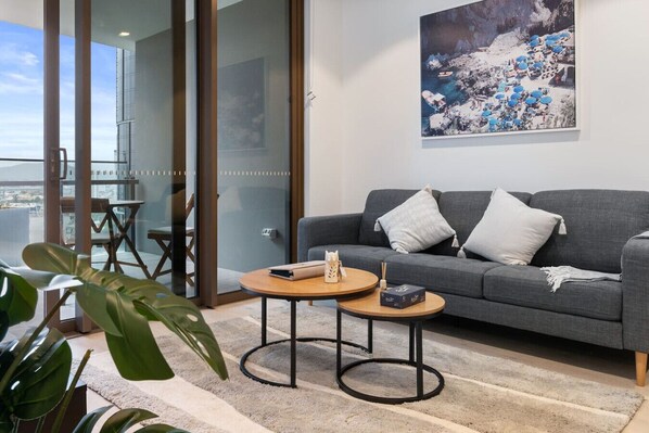 A modern living room with a grey sofa, two round coffee tables, and a large painting of a coastal scene.