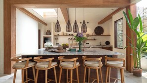 Une cuisine moderne dotée d’un grand îlot central, de tabourets de bar en bois, de luminaires suspendus et de divers accessoires de cuisine.