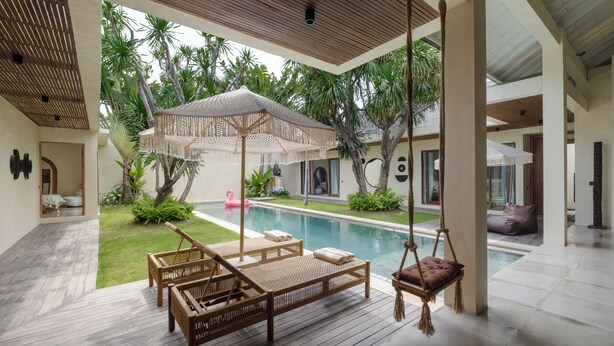 Un espace aménagé au bord de la piscine, avec des meubles en osier, une chaise suspendue et un flotteur en forme de flamant rose.